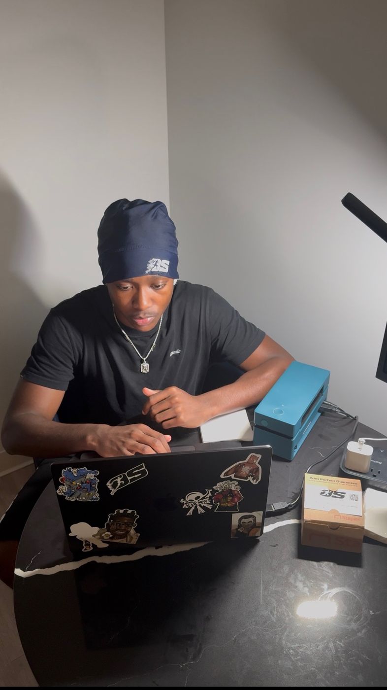 Miles in an OS beanie working on his laptop next to a label printer